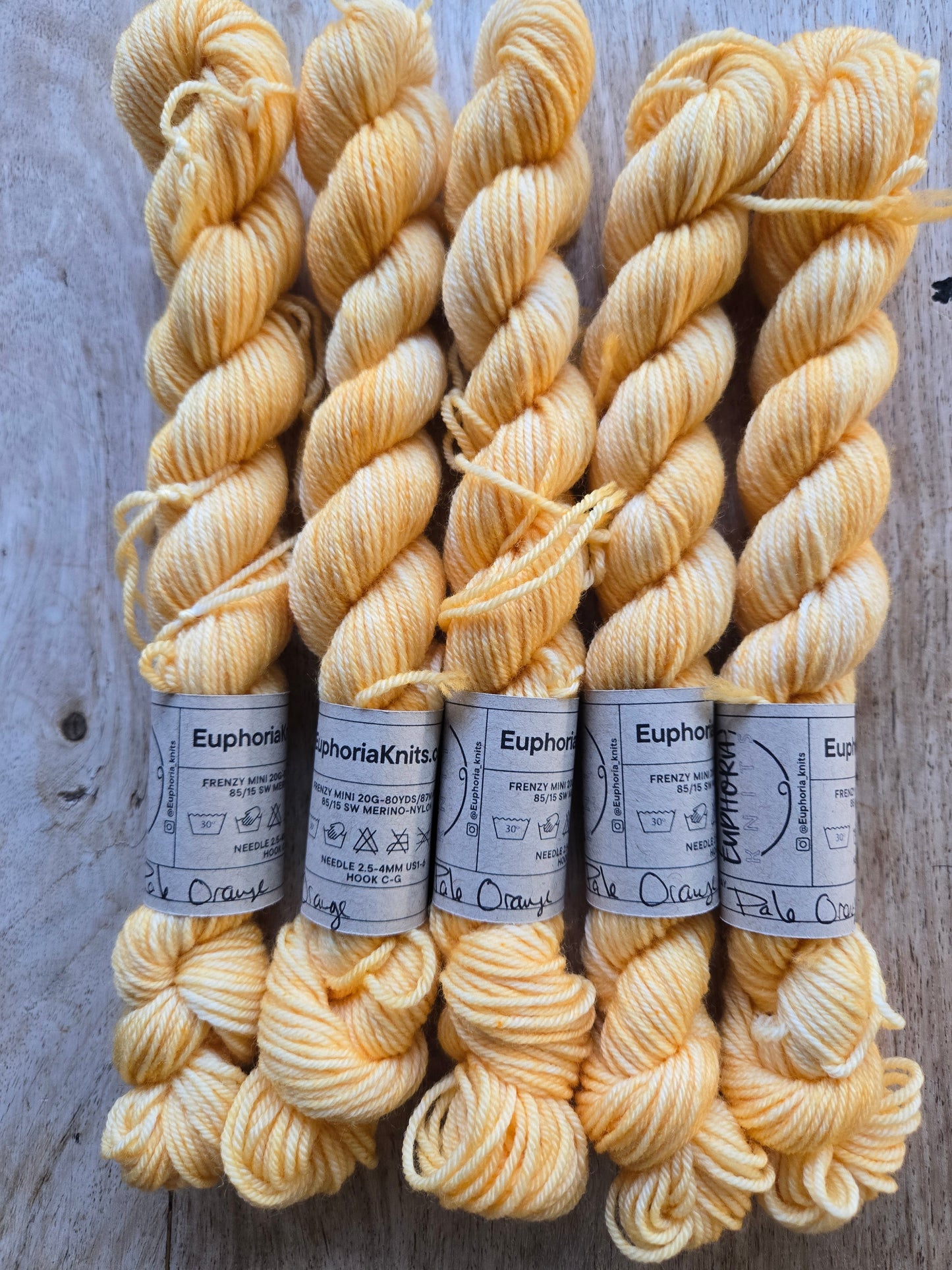 Three skeins of yellow yarn with labels on a wooden surface