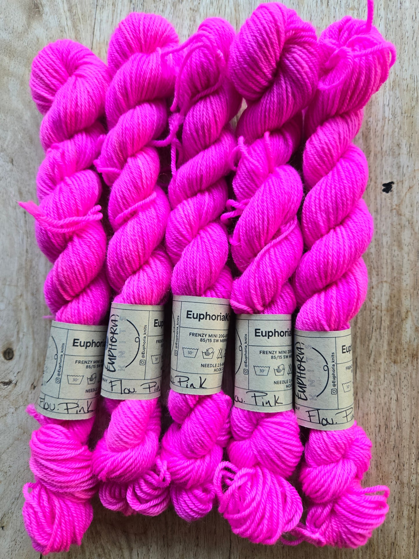 Pink yarn skeins with labels on a wooden surface